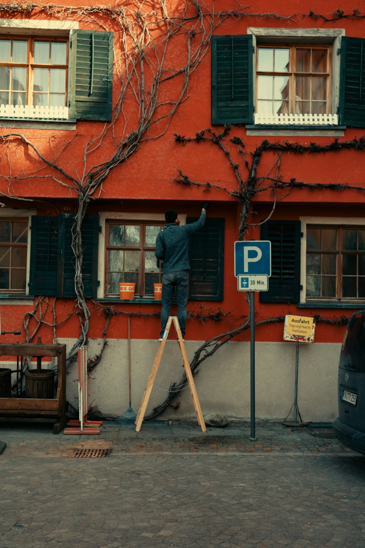 Man painting a red building while standing on a ladder
