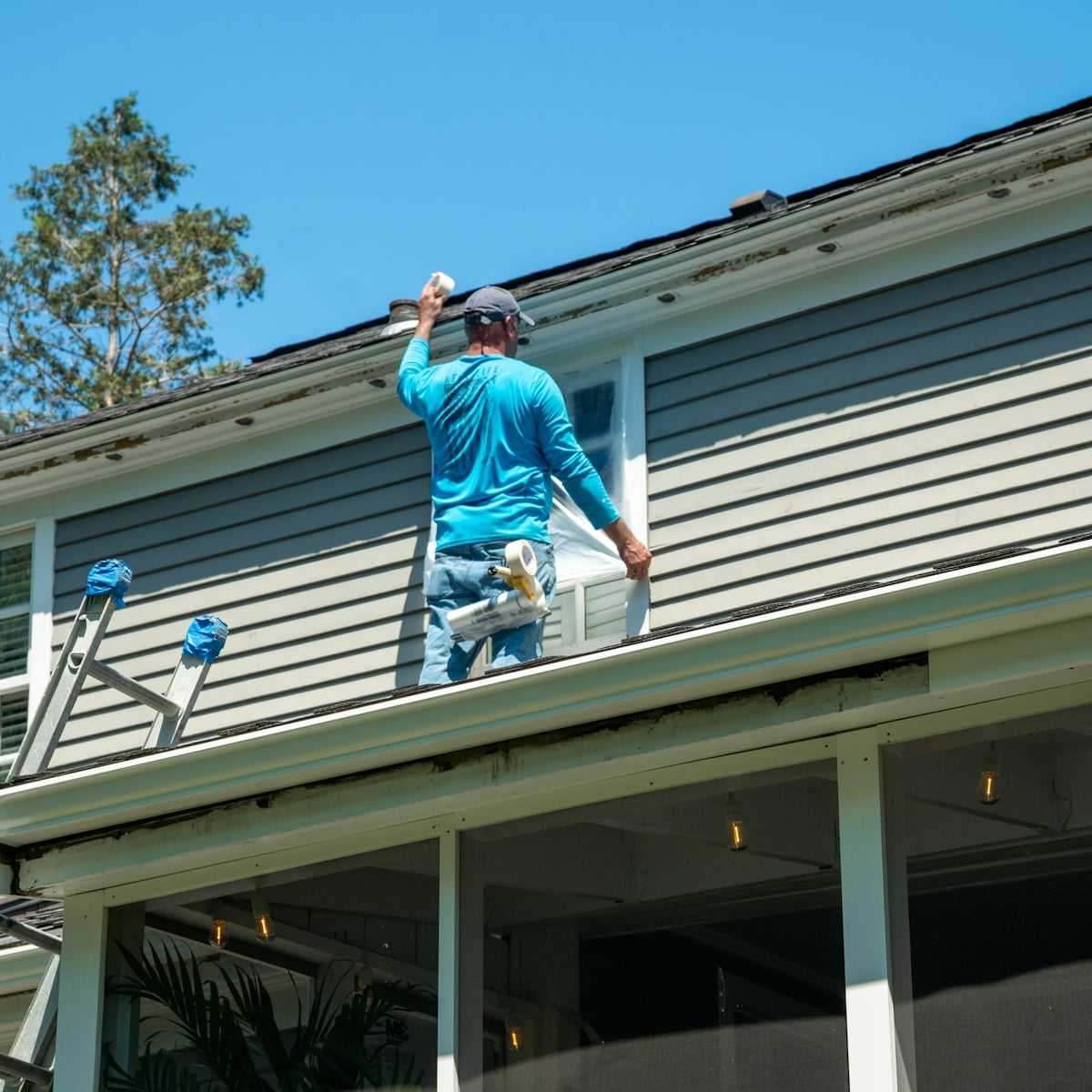 A person in a blue shirt taping plastic over a window on a roof