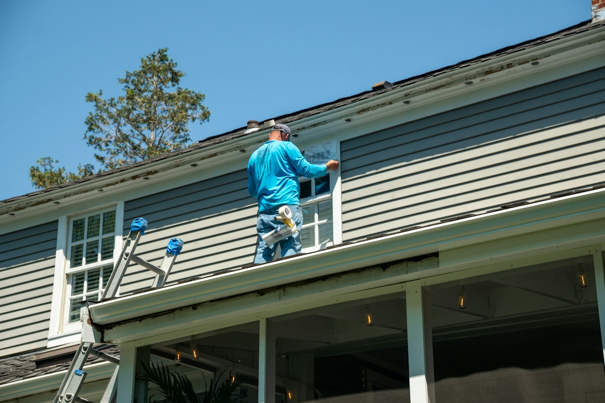 A person in a blue shirt applying tape to a window on a house roof