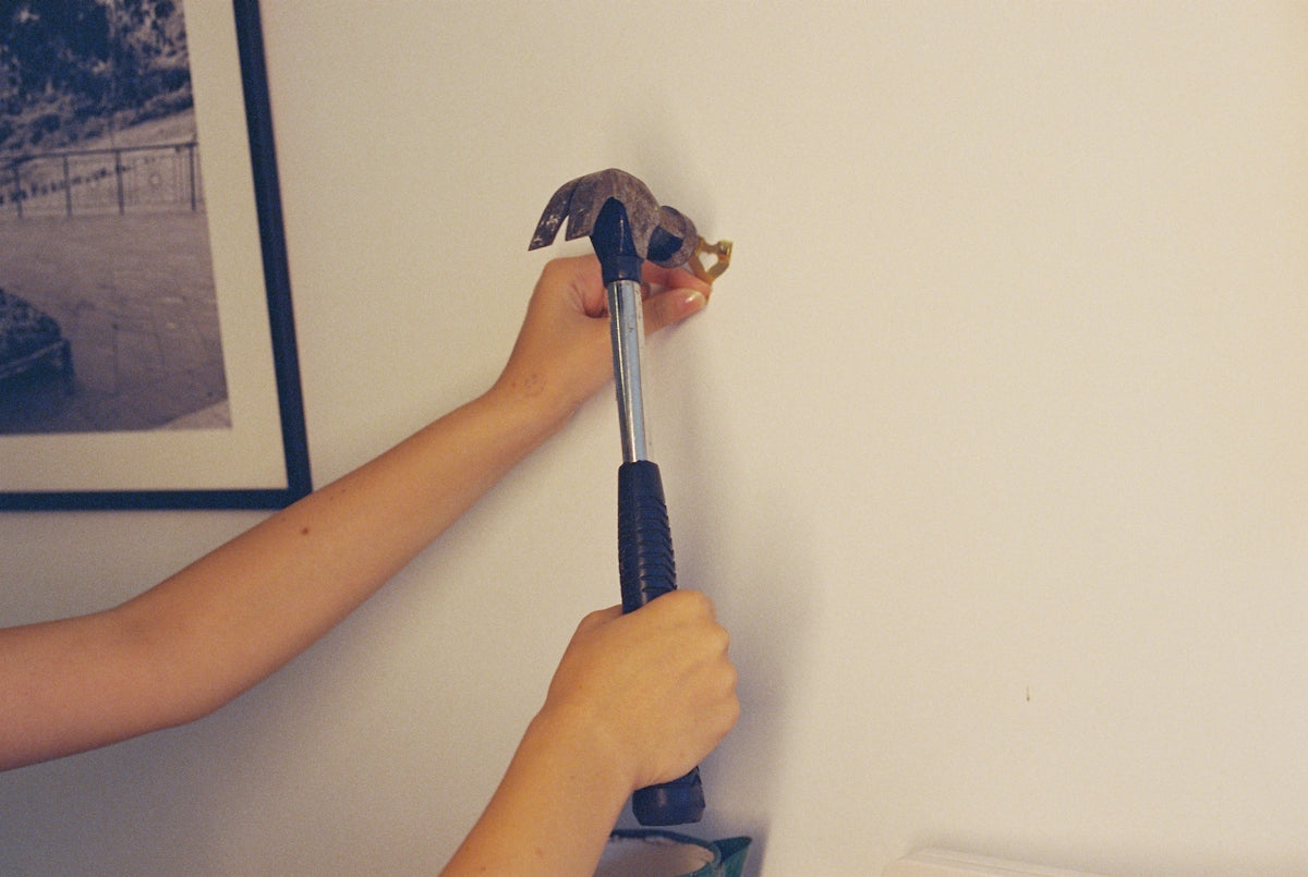 Two hands using a hammer to secure a picture hook on a wall